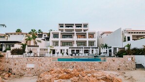 A modern hotel with a pool, multiple balconies, and a stone wall in the foreground.