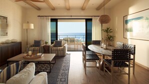 Een ruime woonkamer met uitzicht op de oceaan, met een plafondventilator, een eettafel met stoelen en een bank.