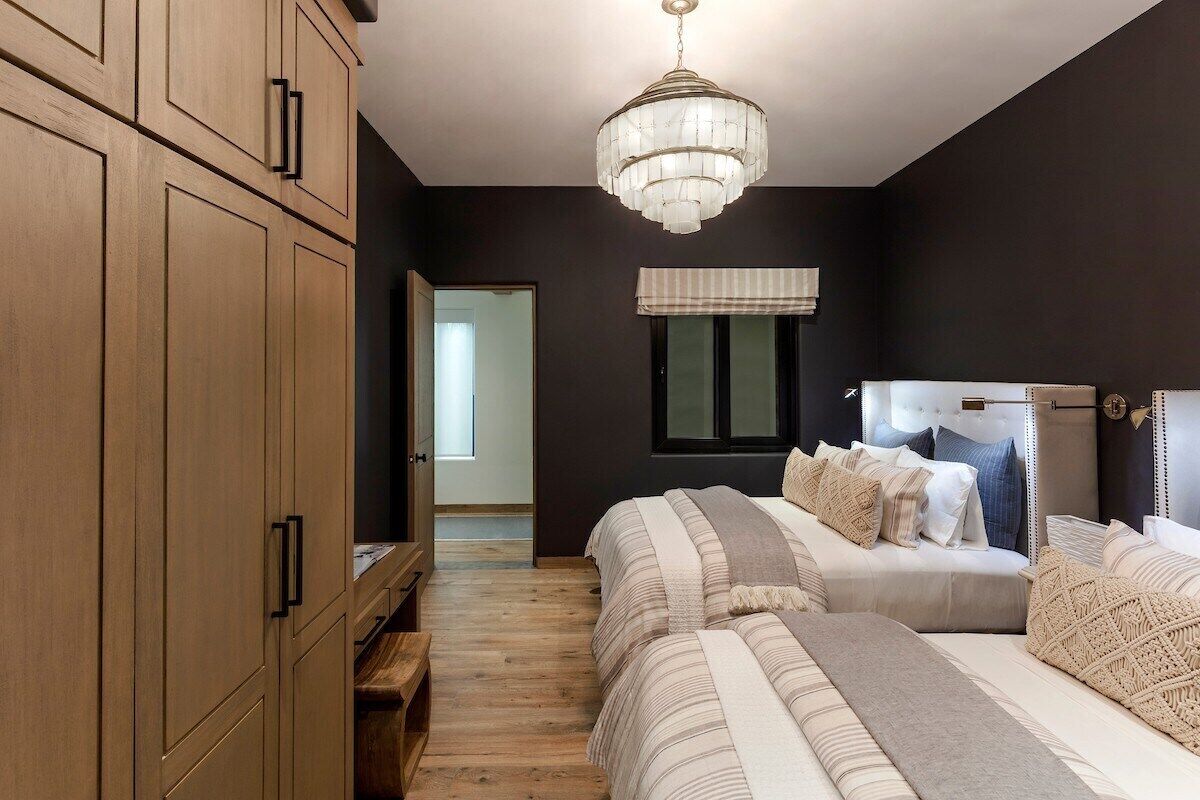 A bedroom with two beds, a wooden wardrobe, a chandelier, and a window with a view.