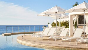 Ein Poolbereich mit Liegestühlen und Sonnenschirmen mit Blick auf den Ozean.