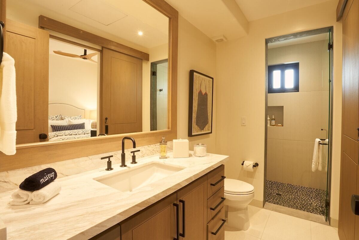 Un baño moderno con un espejo grande, lavamanos dobles, inodoro y ducha a ras de suelo.