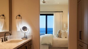 Ein Hotelzimmer mit großem Fenster, einem Bett mit weißer Bettwäsche, einem runden Spiegel und einem Waschbecken mit Marmorplatte.