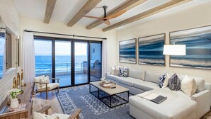 A spacious living room with a large sofa, a coffee table, and a view of the ocean through a sliding glass door. - Oceanfront 2bd penthouse (San José del Cabo)