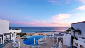 A resort pool area with a view of the ocean, lounge chairs, and umbrellas. - Oceanfront 2bd penthouse (San José del Cabo)