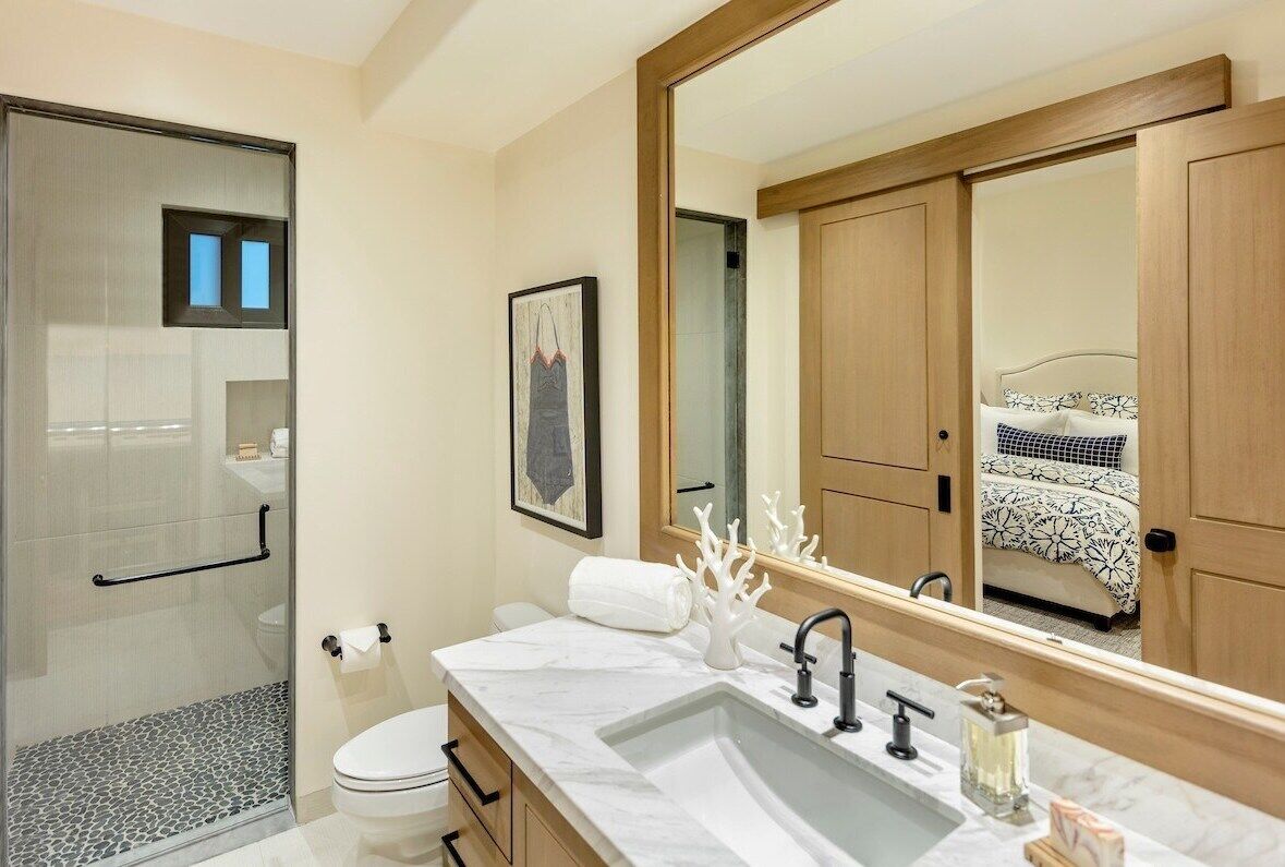 A modern bathroom with a glass shower enclosure, a large mirror, and a marble sink.