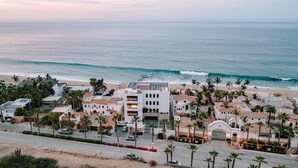Een hotel aan de kust met meerdere gebouwen, een strand op de achtergrond en palmbomen.