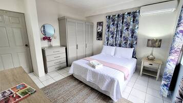 Une chambre à coucher comprenant un lit, une table de chevet, une commode, un miroir, une armoire et une fenêtre avec des rideaux.