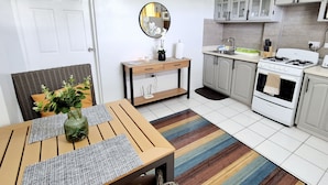 A compact kitchen with a gas stove, oven, and white cabinets. There's a dining table with a placemat and a vase of flowers. - Silver View Apartments (St. George's)