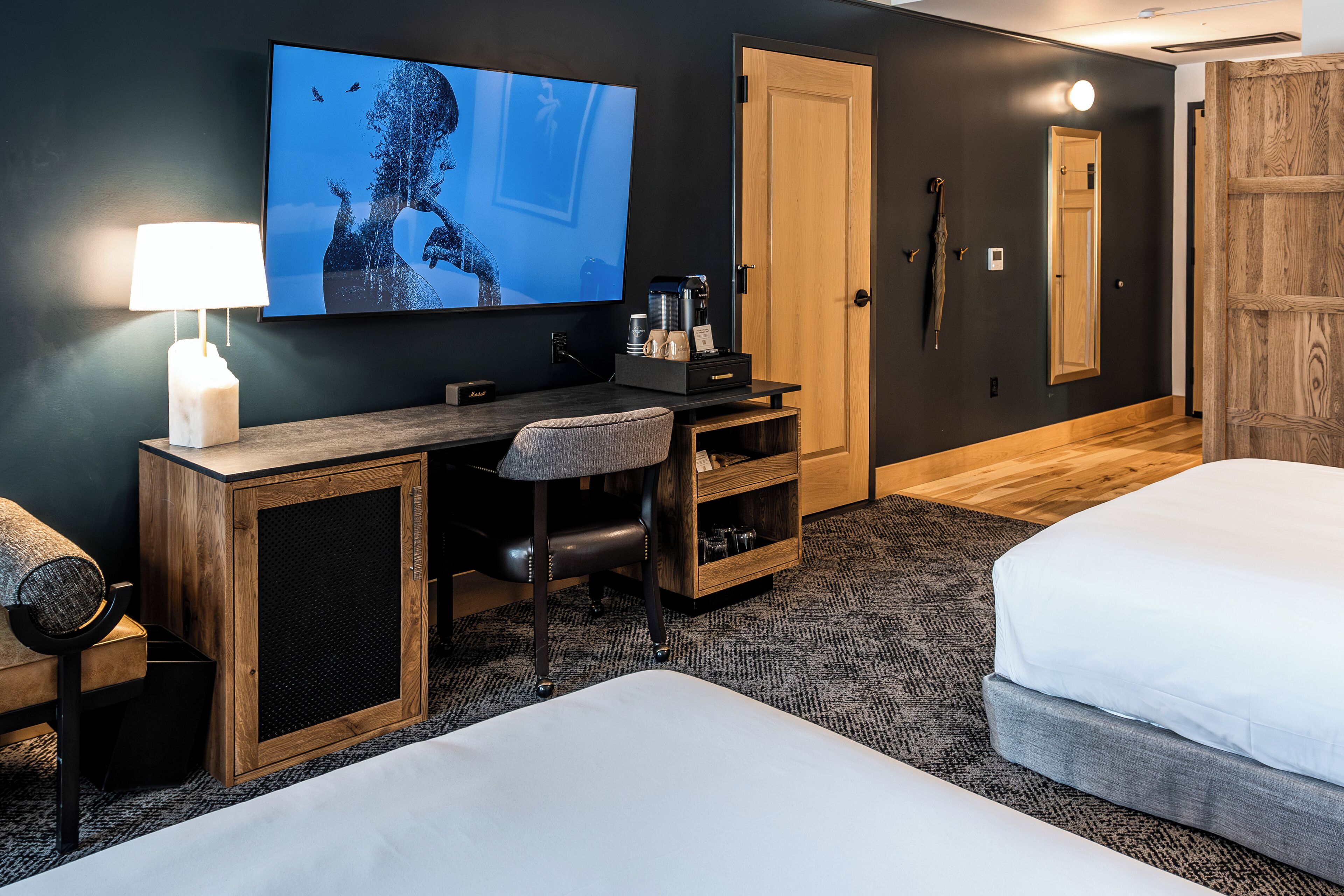 A hotel room with a TV, desk, chair, coffee maker, and two beds.
