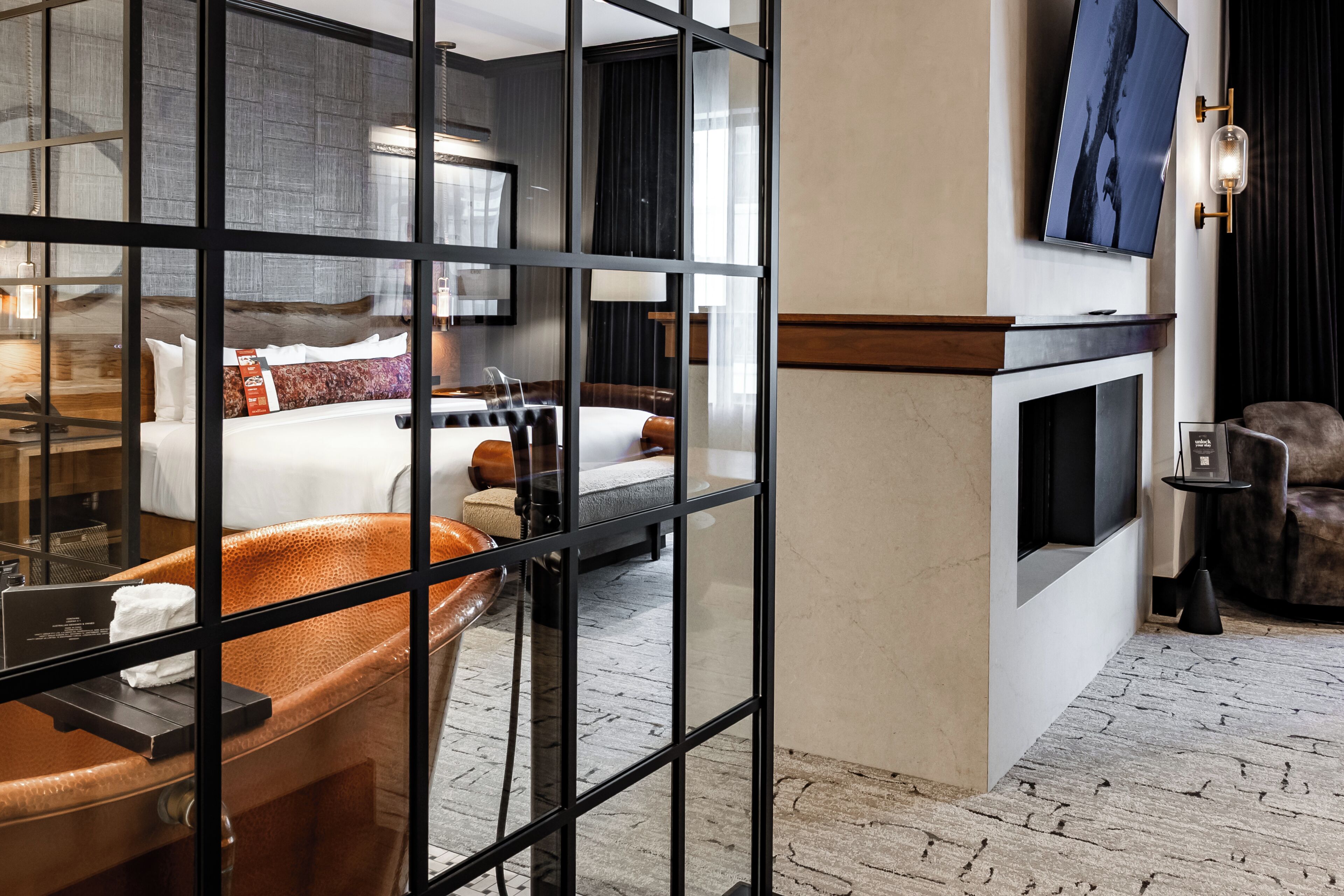 A modern hotel room with a large bed, a bathtub, a television, and a fireplace.
