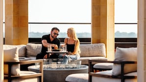 Una pareja cenando en una mesa con vista a la ciudad, rodeada de muebles modernos y una mesa con cubierta de vidrio.