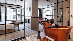 Una habitación de hotel moderna con un ventanal grande, una bañera y una zona de estar con vistas a la ciudad.