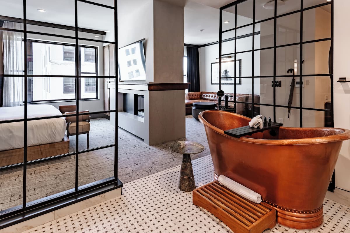 A modern hotel room with a large window, a bathtub, and a seating area with a view of the city.