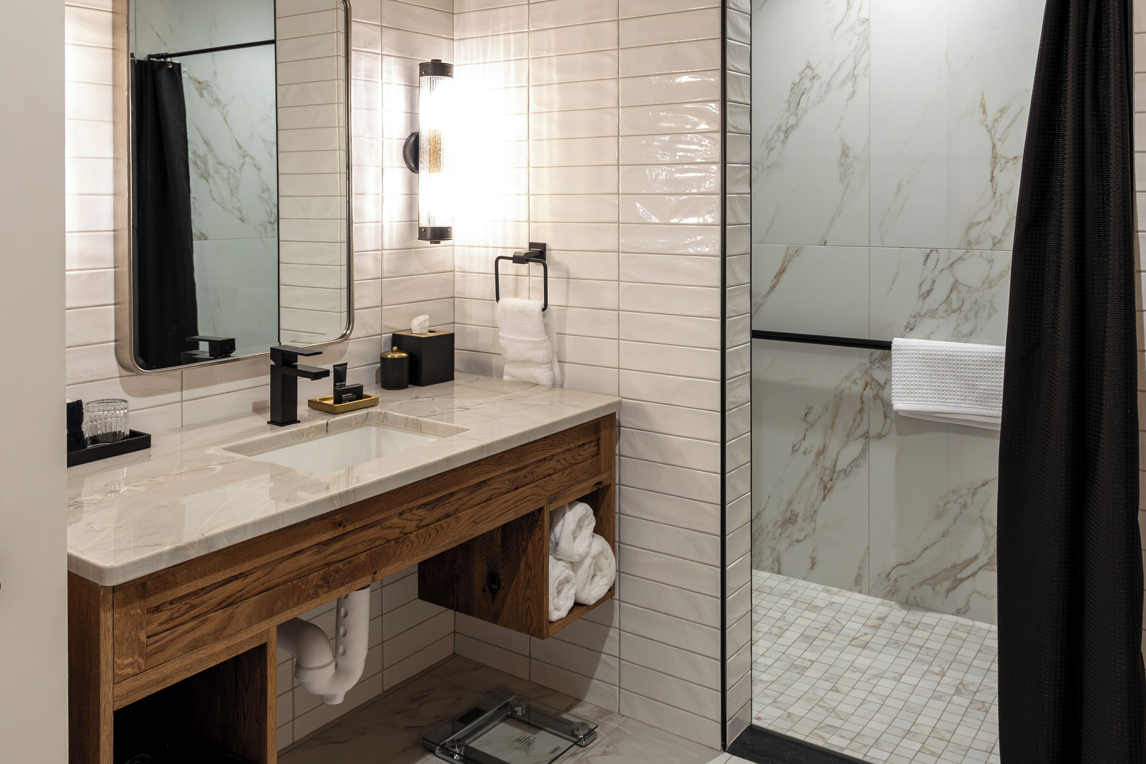 A modern bathroom with a marble-tiled shower, a wooden vanity with a sink, and a large mirror.
