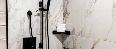 A modern shower area with a wooden bench, marble walls, and black fixtures.