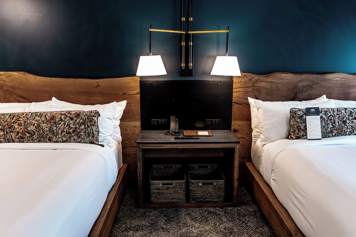 A hotel room with two beds, a nightstand with a lamp, a television, and a small table with a remote control.