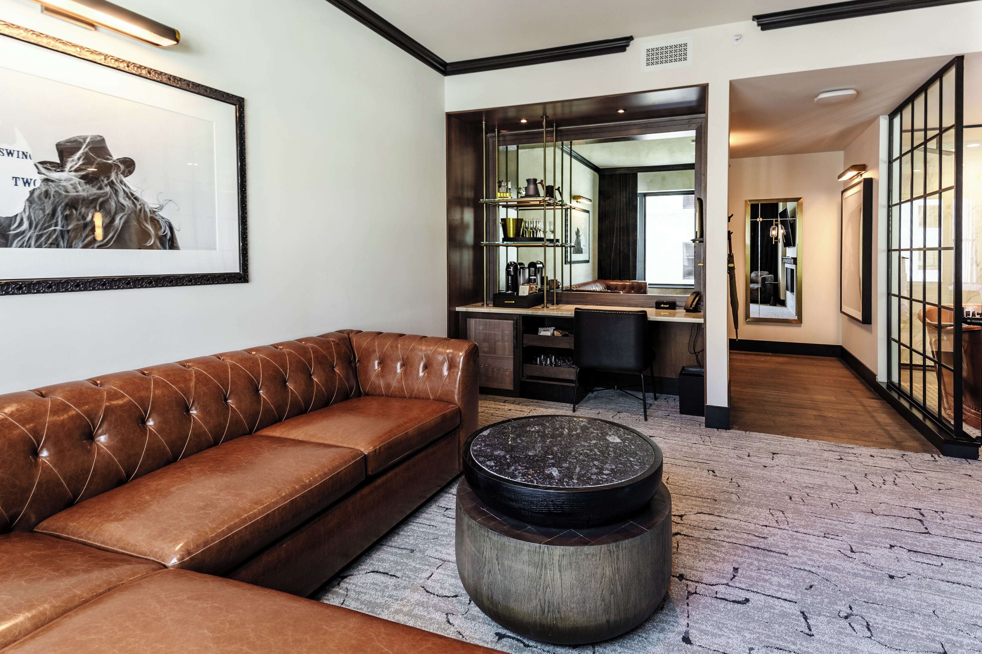 Un salon moderne avec un canapé en cuir marron, une table basse ronde et une œuvre d’art encadrée accrochée au mur.