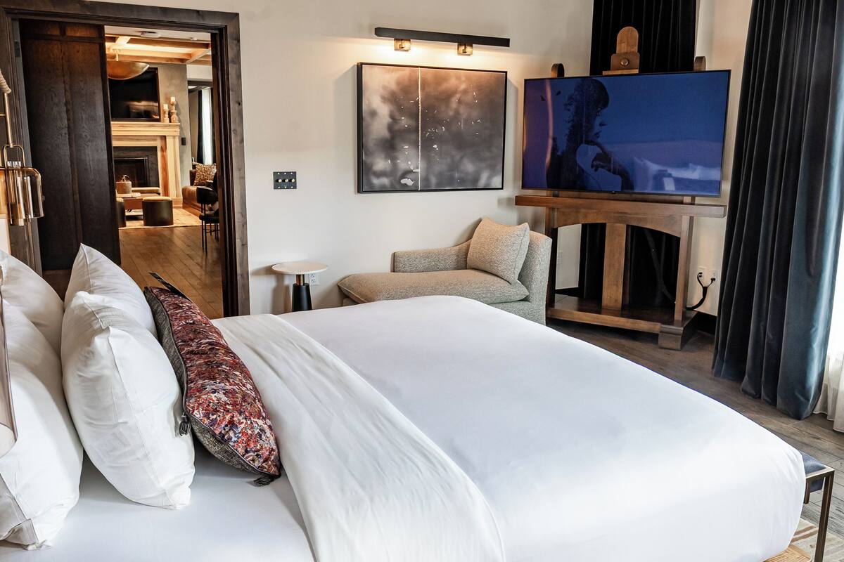A hotel room with a large bed, a TV, a fireplace, and a view of the outside.