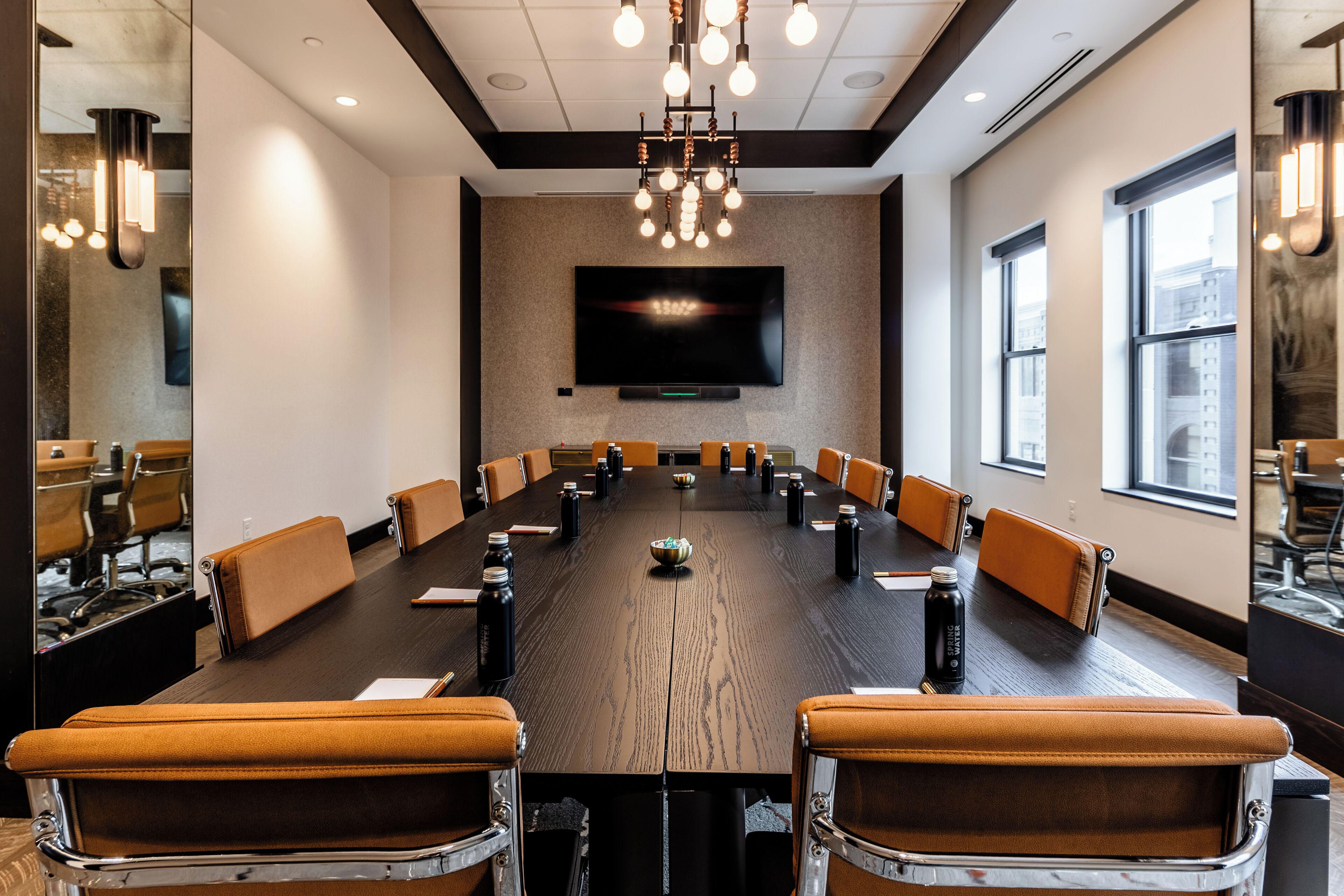 A conference room with a long table, brown leather chairs, and a large flat-screen TV on the wall.