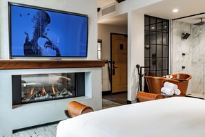 A modern hotel room with a fireplace, a large flat-screen TV, a bathtub, and a shower area. - Hotel Renegade (Boise)