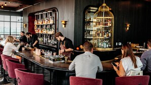 Un bar con una barra larga, sillas rojas y un cantinero.