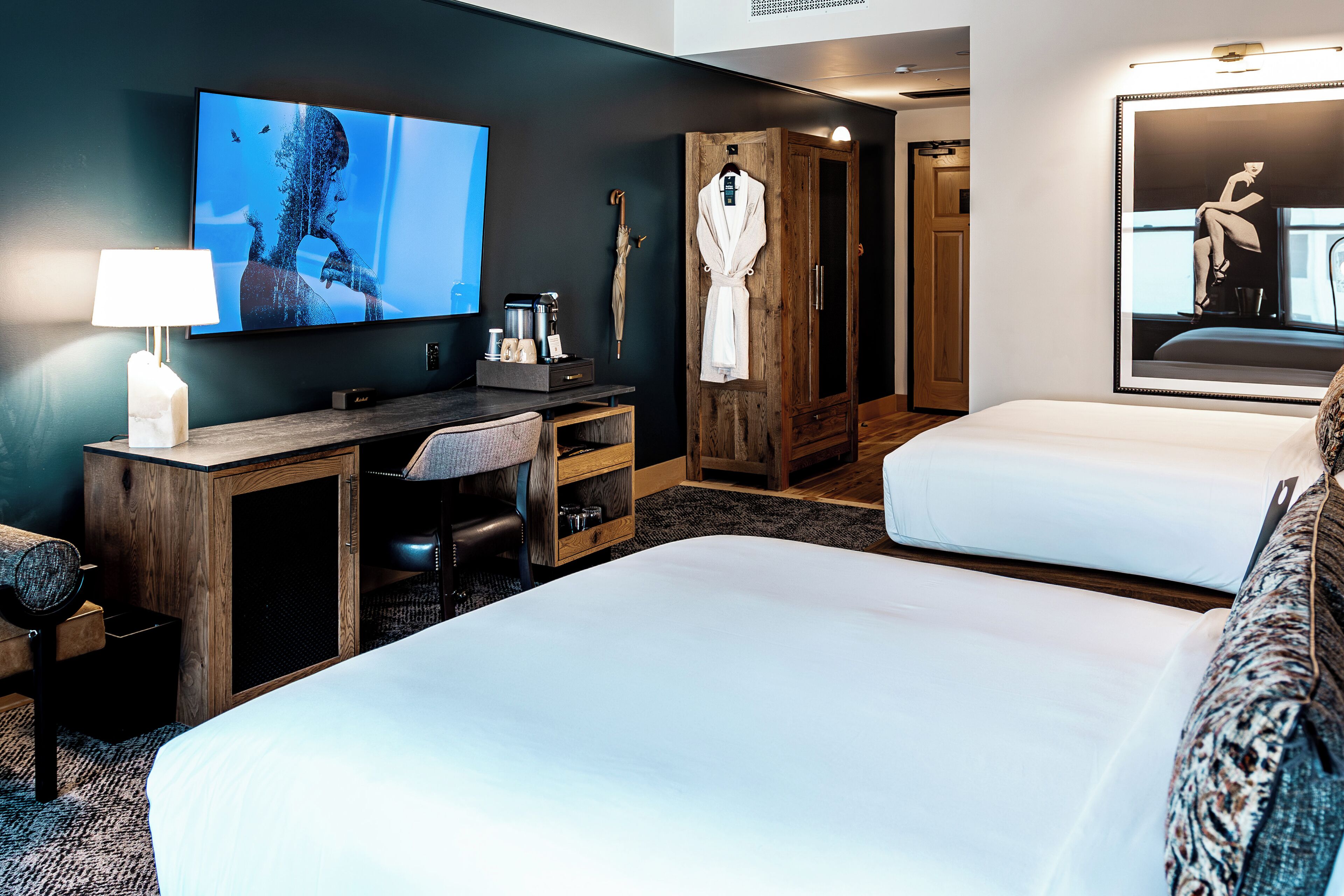 A hotel room with two beds, a desk with a TV, a coffee maker, and a robe hanging on a wooden wardrobe.