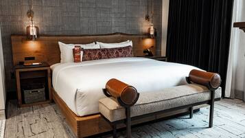 A modern hotel room with a large bed, wooden headboard, two bedside lamps, a bench, and a textured rug.