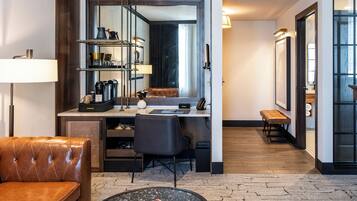 A modern hotel room with a leather sofa, a round coffee table, a desk with a computer, shelves with decorative items, and a large mirror.