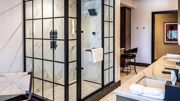 Un baño moderno con ducha envuelta en cristal, encimera de mármol y zona de estar con una silla.