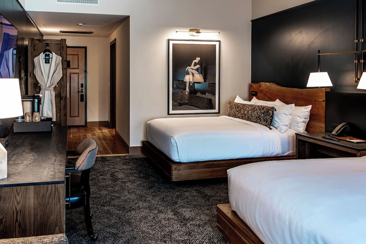 A hotel room with a large bed, a desk with a chair, a robe hanging on the door, and a framed picture on the wall.
