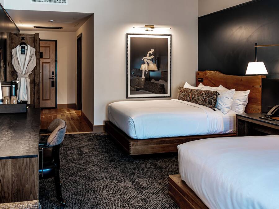 A hotel room with a large bed, a desk with a chair, a robe hanging on the door, and a framed picture on the wall.