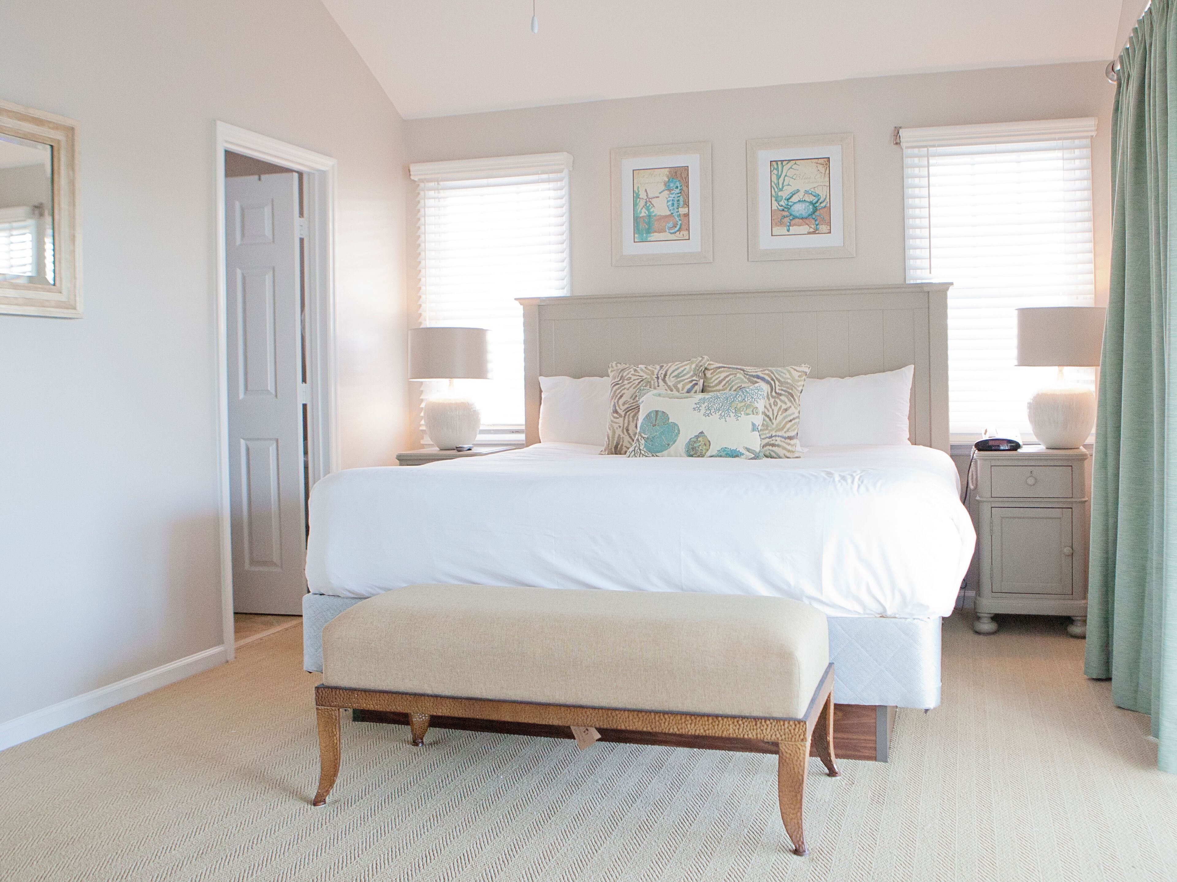 A bedroom with a large bed, a bedside table, a bench, and two framed pictures on the wall.