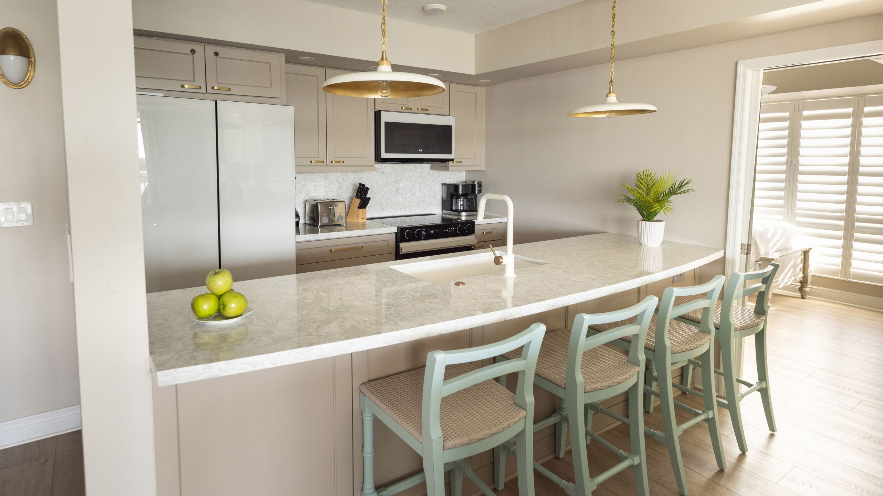 A modern kitchen with a central island, bar stools, a microwave, and a sink.