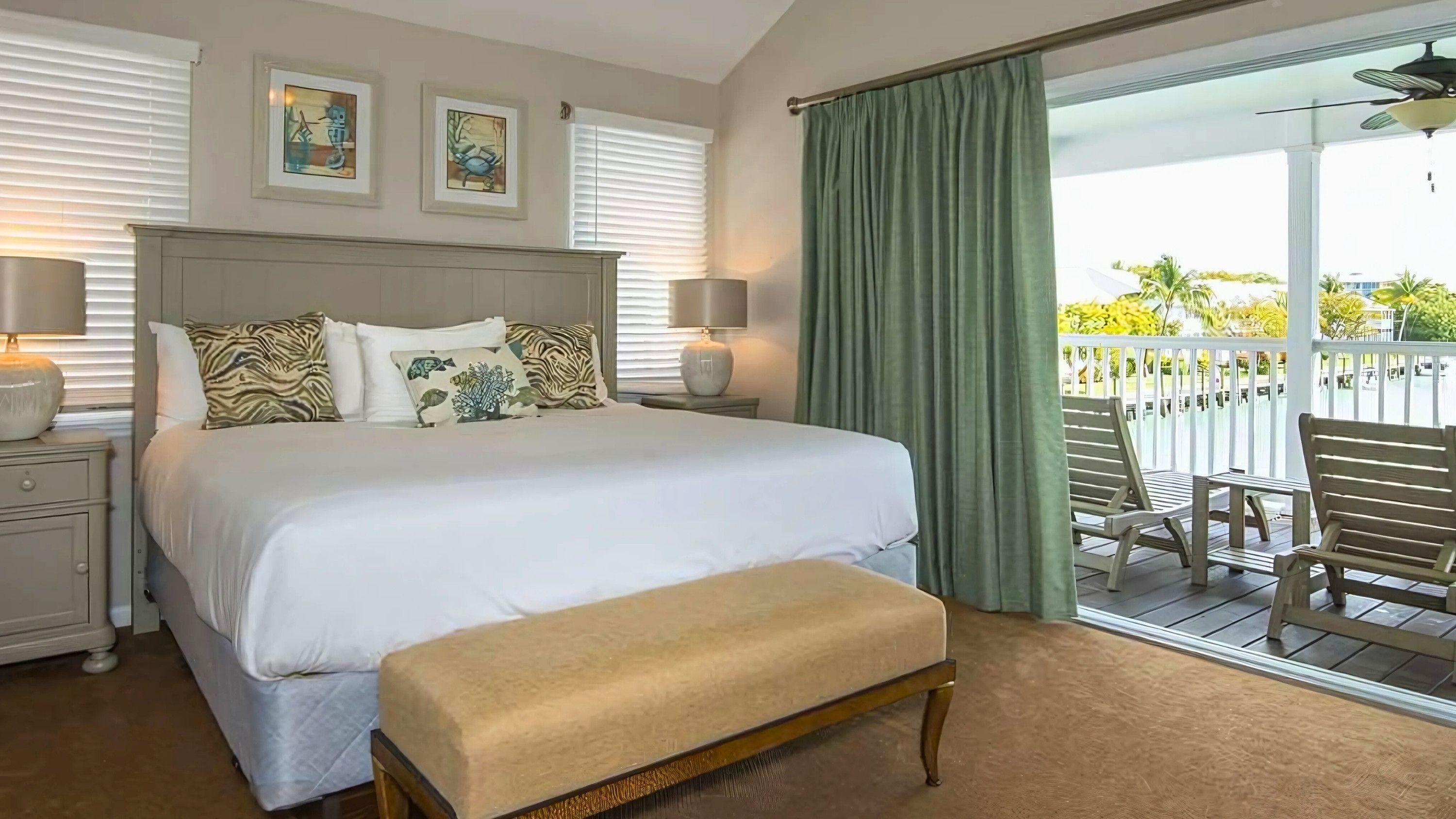 Une chambre d’hôtel avec un grand lit, deux lampes de chevet, un banc et un balcon aménagé avec du mobilier d’extérieur.