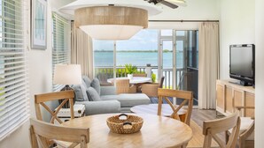 A modern living room with a sofa, chairs, a dining table, a TV, and a view of the ocean. - Villas At Hawks Cay Resort (Marathon)