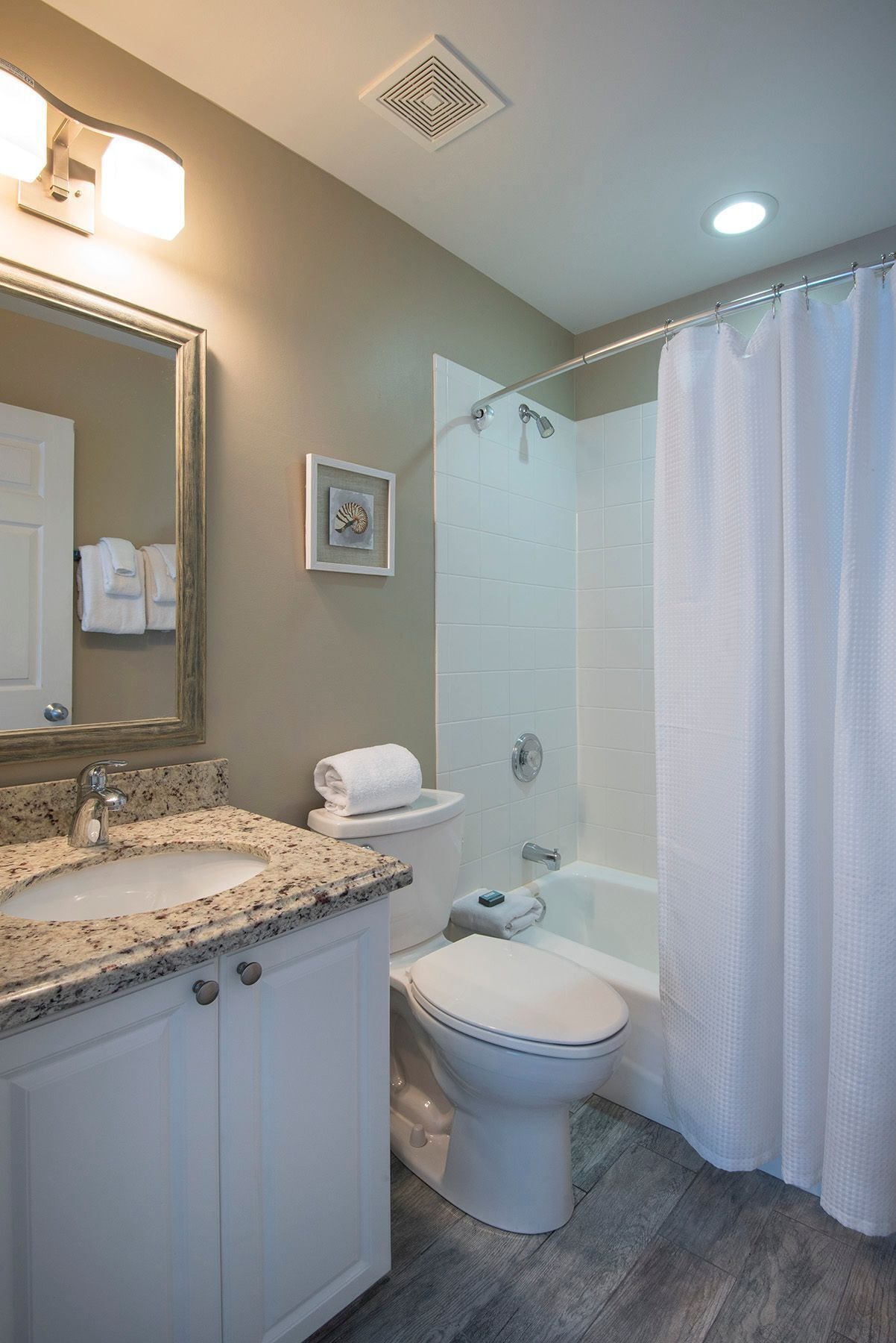 A bathroom with a granite countertop sink, a toilet, a shower with a white curtain, and a ceiling vent.