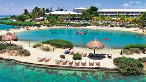 A resort with a large pool surrounded by lounge chairs, a beach area, and a building with multiple floors. - Villas At Hawks Cay Resort (Marathon)