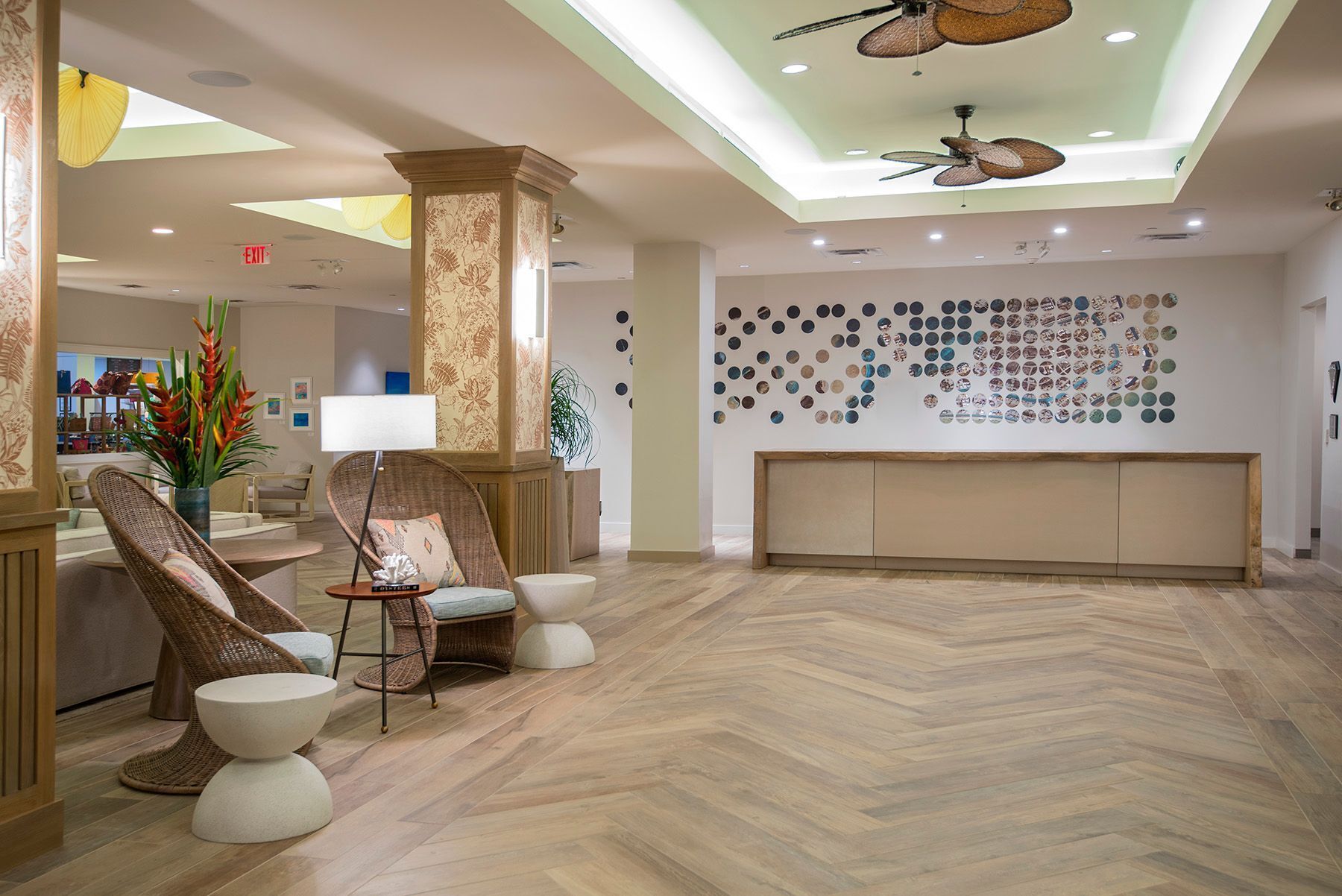 A lobby with a herringbone wood floor, wicker furniture, a reception desk, and a wall of circular mirrors.