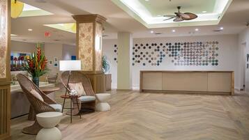 A lobby with a herringbone wood floor, wicker furniture, a reception desk, and a wall of circular mirrors.