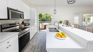 A modern kitchen with white cabinetry, a stainless steel oven, and a large island with a bowl of fruit. - Villas At Hawks Cay Resort (Marathon)