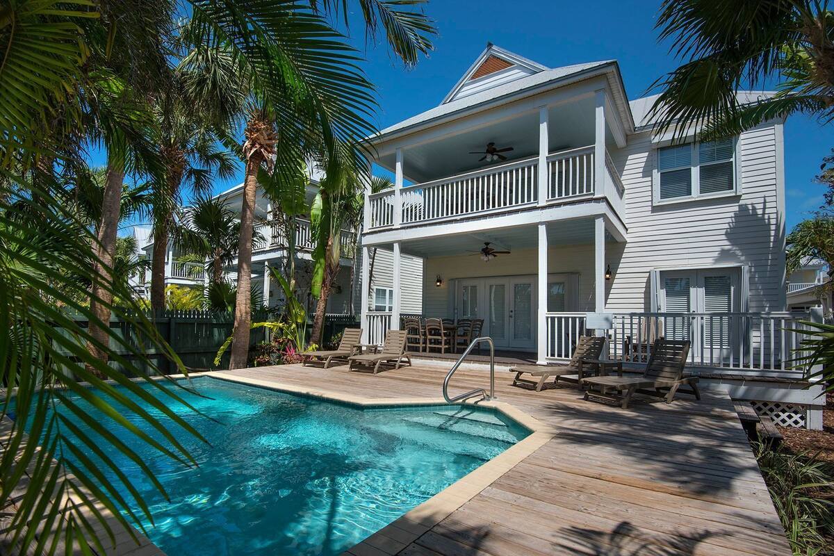 A two-story house with a pool, wooden deck, and outdoor furniture.