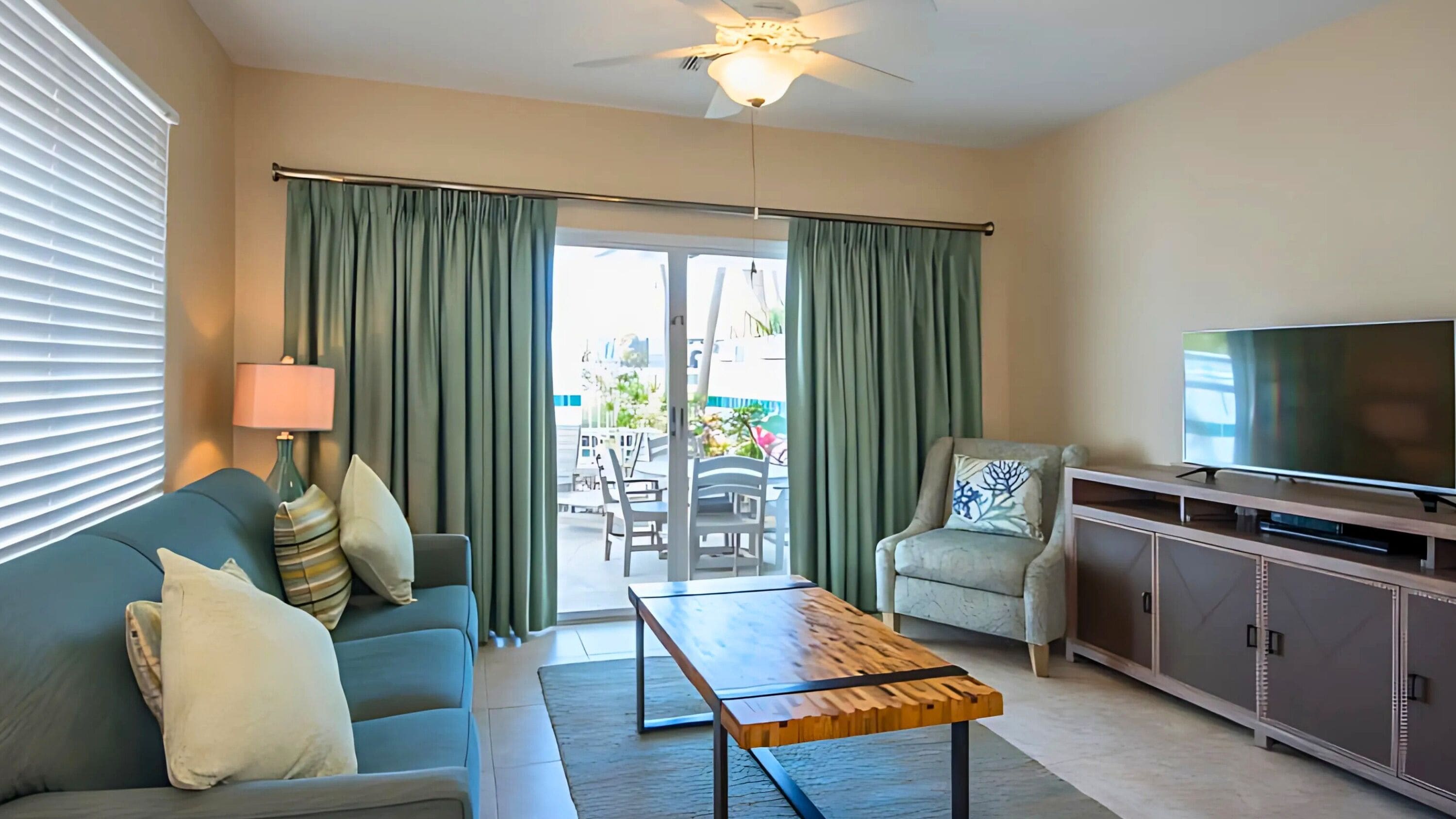 Un salón con sofá, sillón, mesa de centro, televisor y vistas a través de un ventanal.