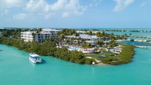 An aerial view of a resort island with a large building, a swimming pool, and a boat docked nearby. - Villas At Hawks Cay Resort (Marathon)