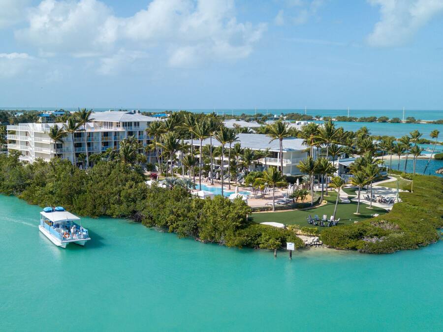 An aerial view of a resort island with a large building, a swimming pool, and a boat docked nearby.