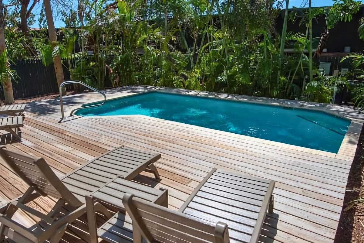 A wooden deck with a swimming pool, surrounded by lush greenery.