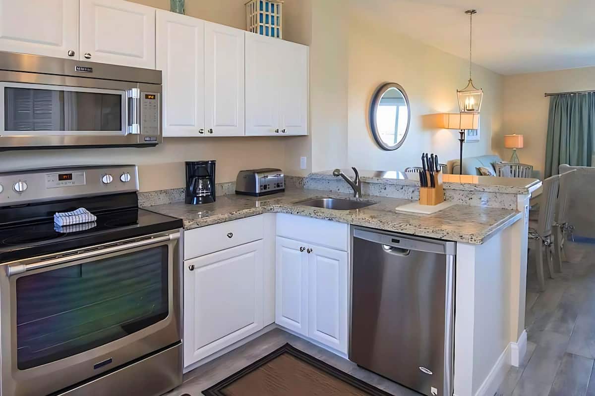 A modern kitchen with stainless steel appliances, white cabinetry, a granite countertop, and a dishwasher.