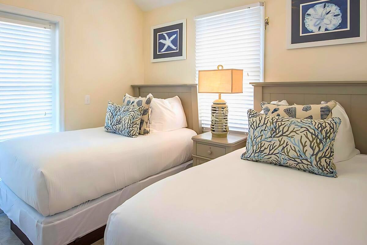 A hotel room with two beds, a nightstand with a lamp, and a wall clock.