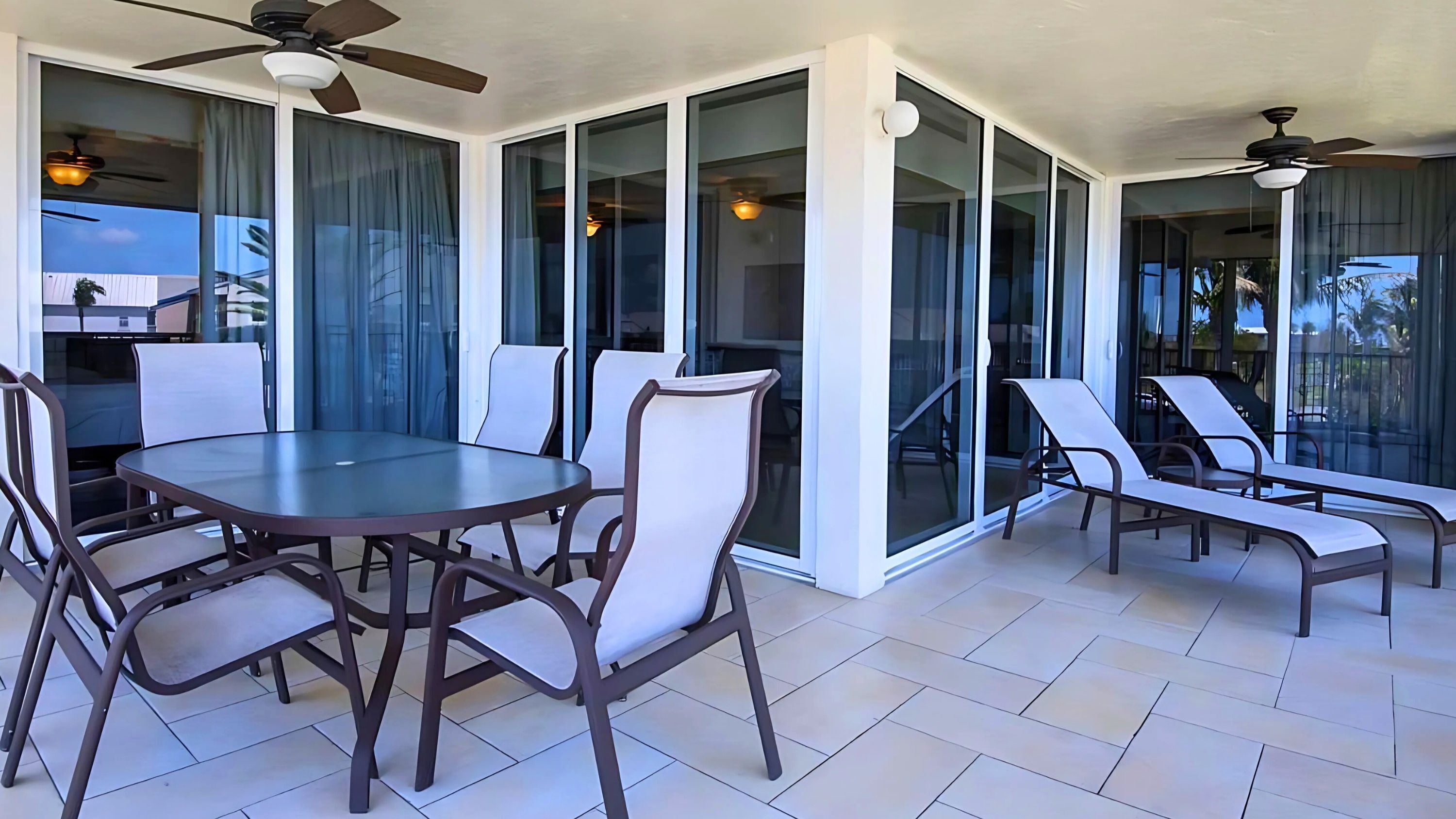 A patio area with a round table and six chairs, large sliding glass doors, ceiling fans, and a tiled floor.