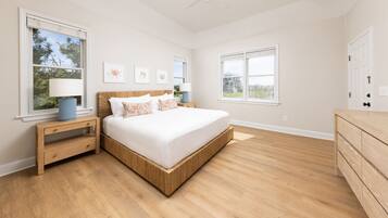 A bedroom with a large bed, wooden nightstands, a dresser, and two windows with blinds.