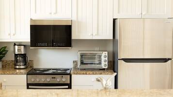 A kitchen with white cabinets, a stove, a microwave, a toaster, and a refrigerator.